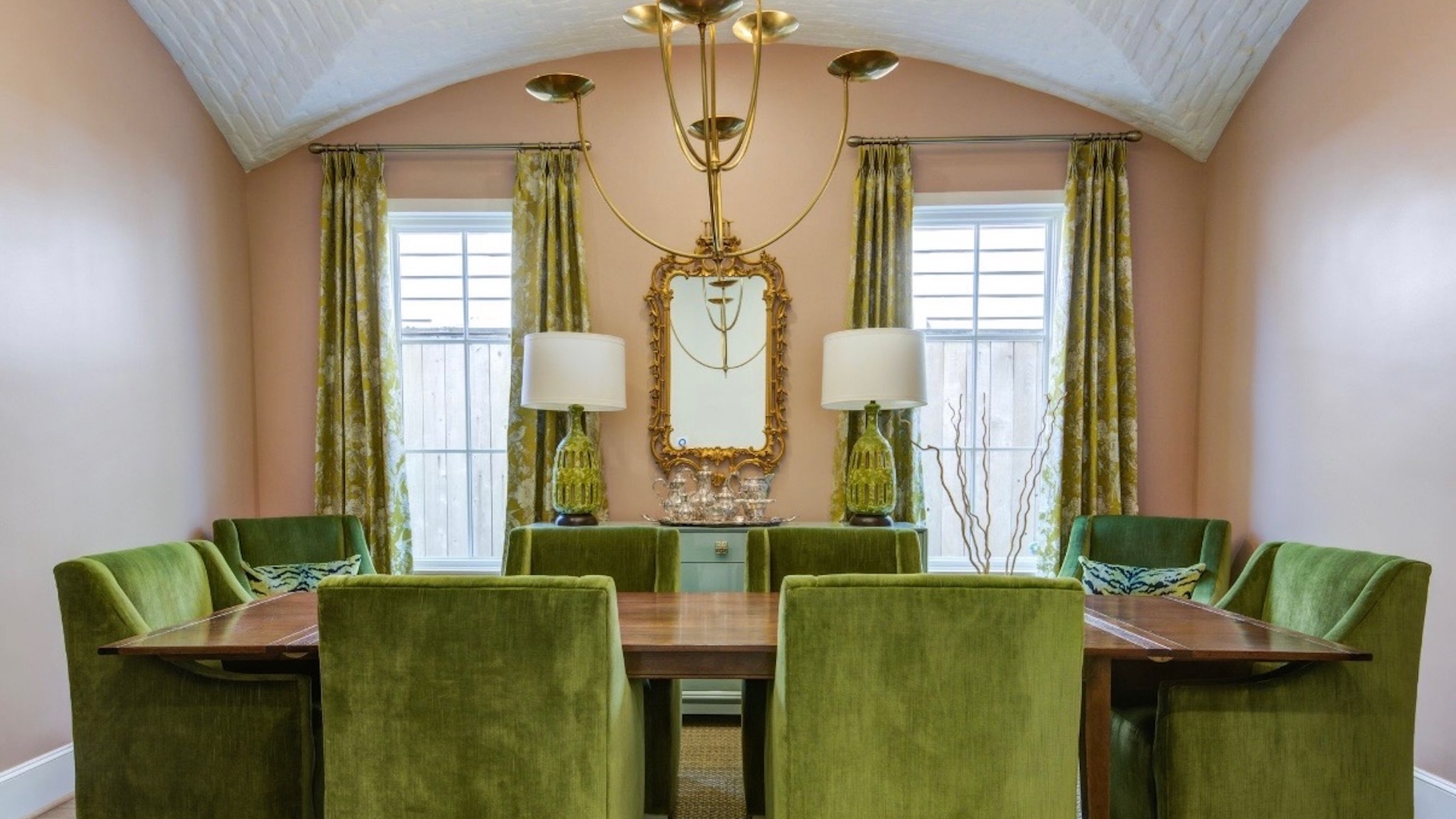 Elegant dining room featuring green upholstered chairs, a wooden table, decorative lighting, and a mirror, reflecting Trinity Construction's commitment to luxury and meticulous design.