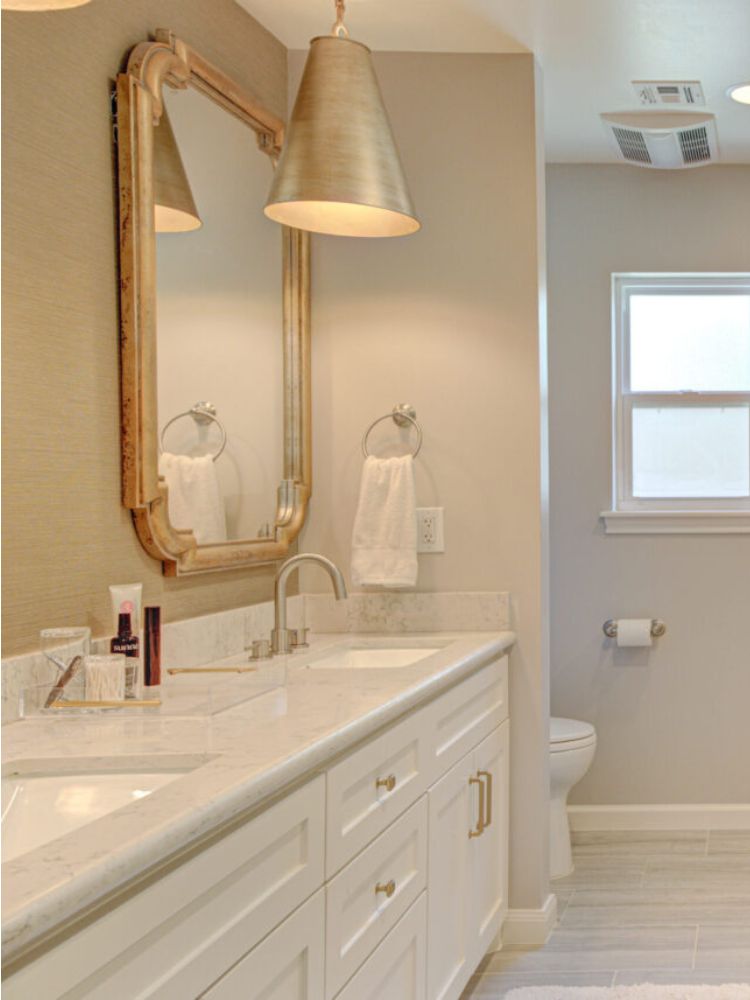 Luxurious bathroom featuring a double vanity with marble countertops, elegant gold fixtures, a large framed mirror, stylish pendant lighting, and modern decor, showcasing Trinity Construction's high-end renovation craftsmanship.